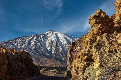 Snow-covered Teide, snowy mountain with road between majestic rocks in clear skies, UNESCO World