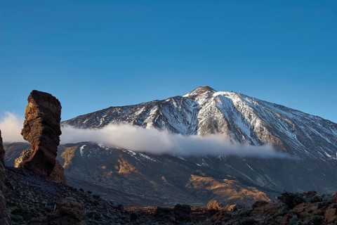 Snow-covered Teide, majestic snowy mountain with rugged rocks in sunlight and clouds above, UNESCO