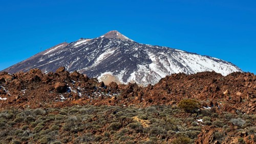 Snow-capped Teide volcano against barren rocky landscape under clear sky, UNESCO World Heritage