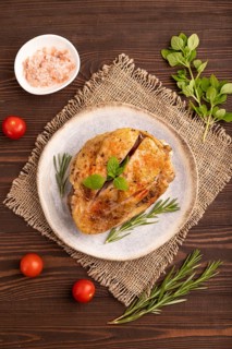 Fried Turkey Thigh with spices and rosemary on plate on brown wooden background and linen textile.