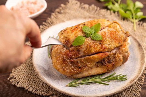 Fried Turkey Thigh with spices and rosemary on plate with hand on brown wooden background and linen