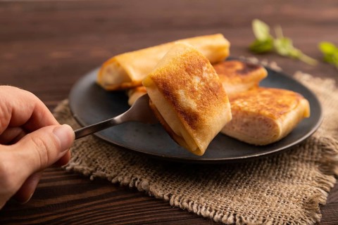 Fried crispy pancakes with meat and cheese with hand on brown wooden background and linen textile.