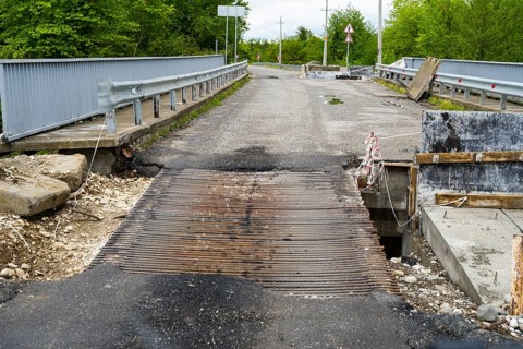 Damaged bridge with metal mesh and surrounding construction in a green area, bridge over the
