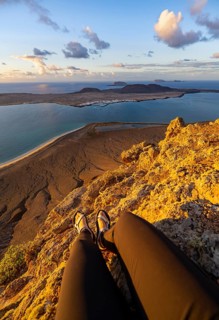 First person view, legs of a woman sitting on a steep cliff, view of the sea and the island of La