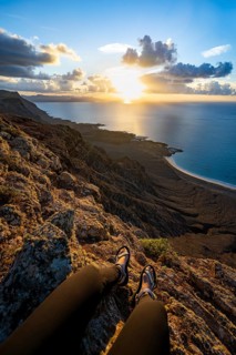 First person view, legs of a woman sitting on a steep cliff, view of sea and coast, Mirador del