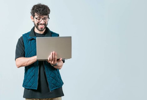 Handsome young man with glasses holding and looking on laptop screen. Portrait of Bearded guy using