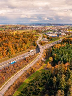 Aerial view of a road in autumn landscape with view of city and wooded area, A8 near Rutesheim,