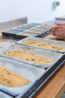 Close-up of dough in loaf pans, hands of a baker visible in the background, Christmas baking,