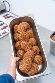 One hand holds a rectangular metal bowl full of brown chocolate chocolates, Christmas baking,