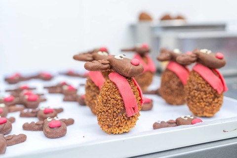 A tray full of reindeer cookies with red noses and scarves in a bakery, Christmas baking,