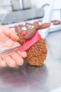 Hand sculpting a chocolate reindeer praline with red scarf and nose, Christmas baking, Haselstaller