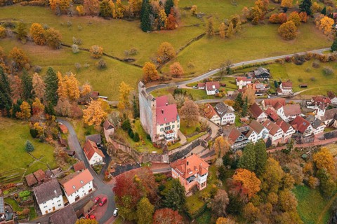 A historic castle towers over an autumnal village in extensive meadows, Berneck Castle,