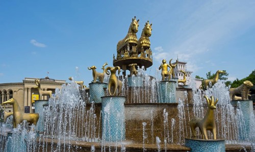 Golden horses and ram statues surrounded by water fountains against an architectural backdrop,