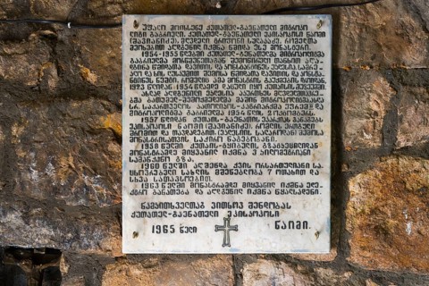 A plaque on a stone wall inscribed with religious text, a cross below, memorial plaque dedicated to
