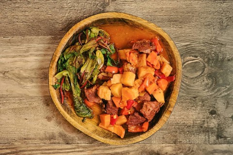 A warm bowl of beef stew features tender chunks of meat, potatoes, carrots, and bell peppers.