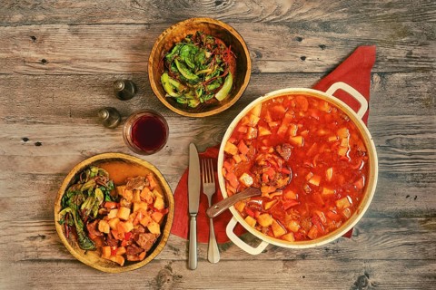 A large pot of beef stew on a wooden tabletop. Portion of beef stew is served on a rustic wooden