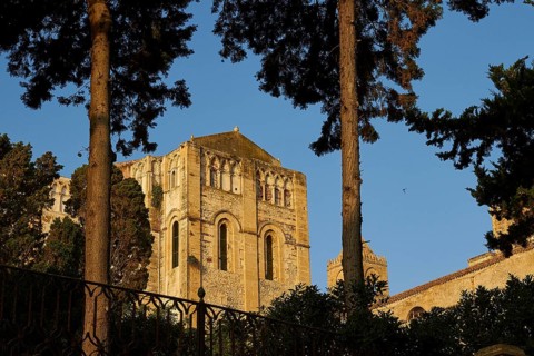 Historic Romanesque church surrounded by trees under clear blue sky at sunset, Cefalu, cathedral,