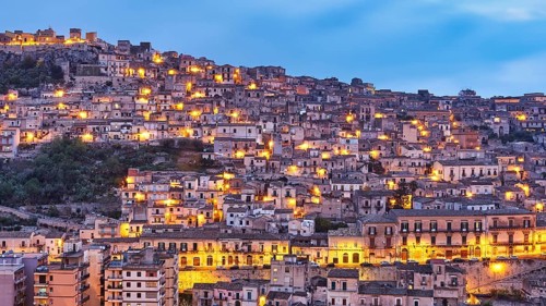 Modica, evening view of a mountainous urban landscape with illuminated houses, Baroque towns of