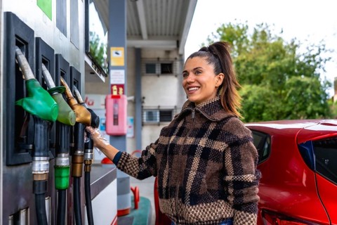 Woman smiling and wearing a protective glove while selecting a fuel pump to refuel her red car at a