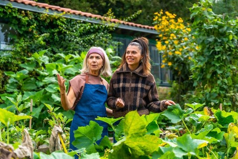 Mother and adult daughter enjoying time together in a lush green garden, the older woman teaching