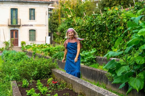 Senior woman smiling while walking through her bountiful urban vegetable garden, cultivating fresh