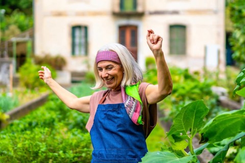 Happy senior woman dancing with arms raised in her home garden, celebrating an active and joyful