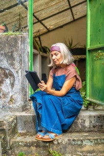 Senior woman in denim overalls and headband sits on rustic outdoor steps in a garden, focused on a
