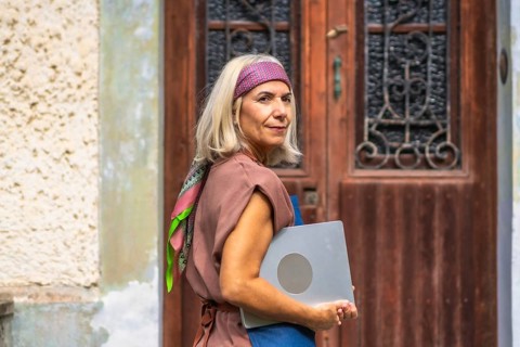 Senior woman with gray hair wearing a headband and casual outfit, carrying a laptop and looking