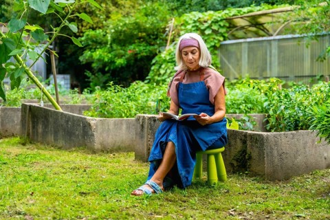 Senior woman wearing an apron and headband, enjoying a quiet moment reading a book while sitting on