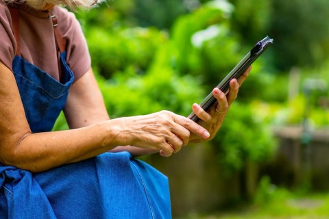 Senior woman is holding and interacting with a digital tablet in a vibrant green garden, embracing