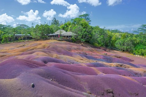 Colourful red and purple dunes in front of a tropical forest under blue skies in Mauritius. Africa,