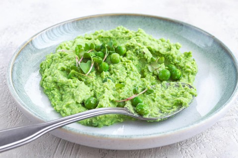 A vibrant green pea puree fills a shallow bowl, topped with fresh peas and microgreens. The dish