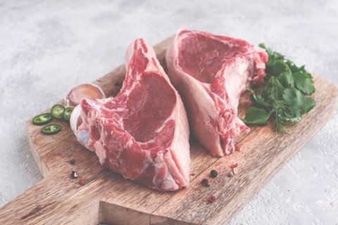 Fresh pieces of beef on the bone, on a wooden cutting board, with herbs and spices, ready for
