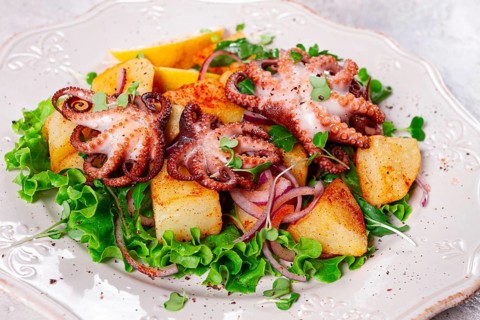 Grilled octopus with baked potatoes and fresh herbs, on a decorative light plate, homemade, no
