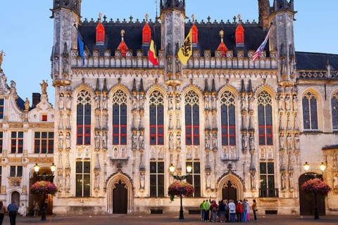Tourist group looking at illuminated historic town hall of Bruges on Castle Square in the evening