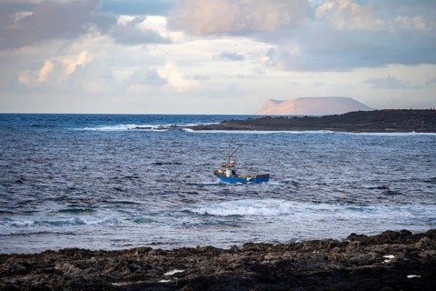 Fishing boat out to sea in the evening, seaside coast with volcanic rocks at sunset, La Santa,