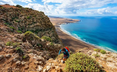 Female hiker climbing to Castillejo summit, view from the Risco de Famara cliffs of the coast and