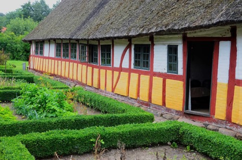 Half-timbered house with thatched roof by an older kitchen garden with boxwood hedges in Den gamle