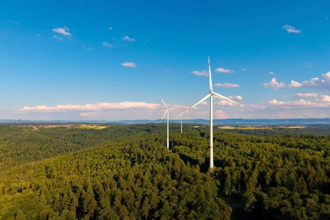 Green forests with several wind power plants under vivid blue sky with clouds, near Schorndorf,