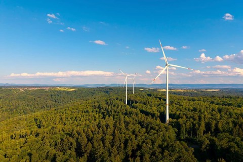 Wind turbines over green forest area, surrounded by beautiful clouds under a blue sky, near