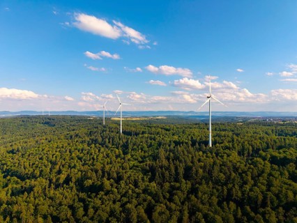 Several wind turbines rise above a lush forest under a sky with light clouds, near Schorndorf,