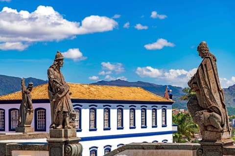 Statues of biblical prophets sculpted by Aleijadinho with ancient buildings and mountains in the