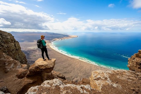 Young woman enjoying the view from the Risco de Famara cliffs to Famara beach, Playa de Famara with
