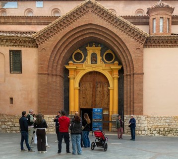 Tour guide and group of people outside Mudéjar door of cathedral church building, city centre of