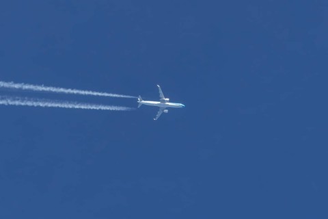 Jet passenger aircraft flying in a blue sky with contrails or vapour trails behind, England, United
