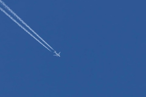 Airbus jet passenger aircraft flying in a blue sky with contrails or vapour trails behind, England,