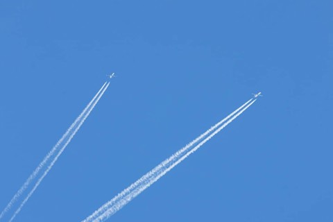 Two jet passenger aircraft flying in a blue sky with contrails or vapour trails behind, England,