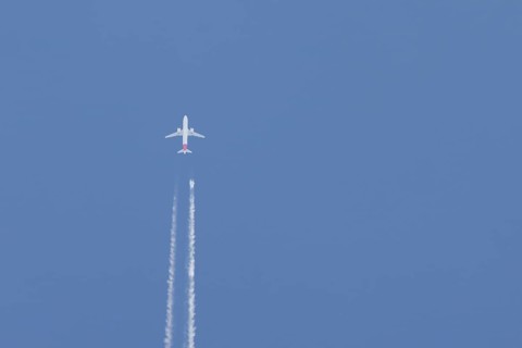 Airbus jet passenger aircraft flying in a blue sky with contrails or vapour trails behind, England,