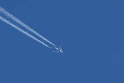 Boeing 777 jet cargo aircraft of FedEx Express airlines flying in a blue sky with contrails or