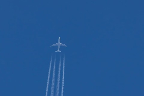 Jet commercial passenger aircraft flying in a blue sky with contrails or vapour trails behind,